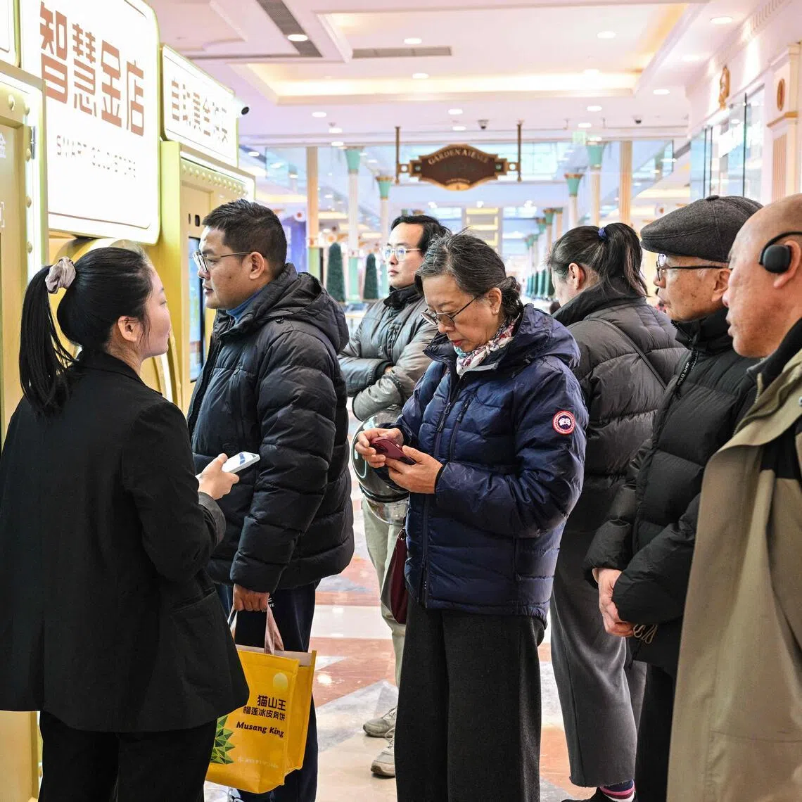 Customers wait to sell their gold jewelry in a Smart Gold Store Machine placed in a shopping in Shanghai on January 29, 2026. Dozens of people crowded around an automated gold recycling machine at a Shanghai mall, hoping to melt down family heirlooms for cash as prices of the precious metal hit record highs. (Photo by Hector RETAMAL / AFP) / TO GO WITH: China-economy-gold, by Jing Xuan Teng