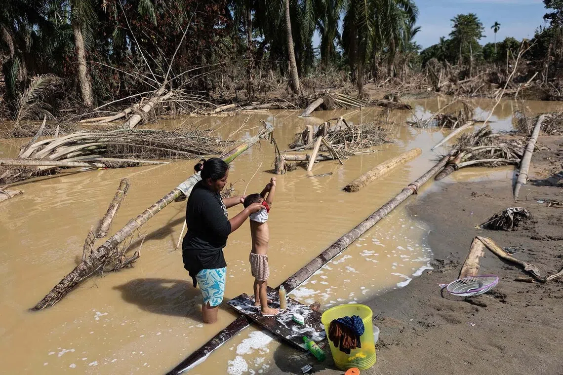 A mother bathing her child in muddy waters amid a clean water shortage in the aftermath of flash floods at Aceh Tamiang in Northern Sumatra on Dec 10, 2025.