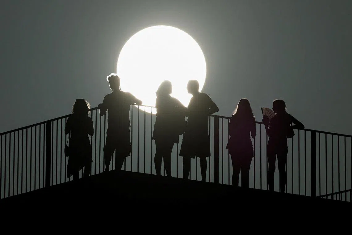 A tourist cools herself off with a fan, as people are silhouetted against the strong sun, during sunset at the Aldehuela lookout, amid the third heatwave of the summer, in Ronda, Spain August 11, 2023. REUTERS/Jon Nazca