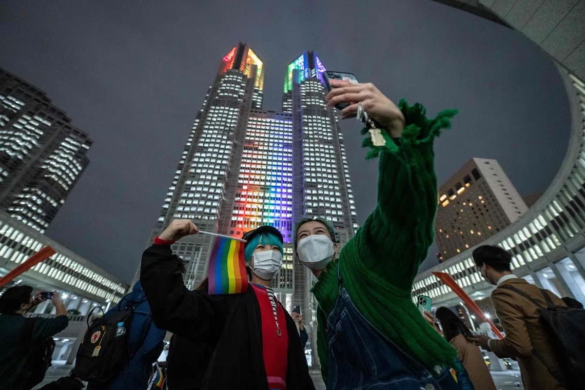 People take selfie in front of the Tokyo Metropolitan Government building illuminated with rainbow lights in Shinjuku district of Tokyo on November 1, 2022. - Tokyo began issuing partnership certificates to same-sex couples who live and work in the capital on November 1, a long-awaited move in a country without marriage equality. (Photo by Yuichi YAMAZAKI / AFP)