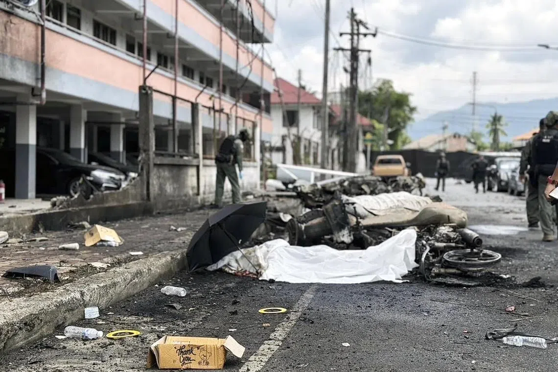 epa11446853 The covered dead body of a victim lies next to a destroyed vehicle as members of the Explosive Ordnance Disposal (EOD) unit and forensic police officers inspect the scene of a bomb blast, after a car exploded in front of a police flat in Bannang Sata district, Yala province, southern Thailand, 30 June 2024. According to the police, a woman was killed while 18 others, including 8 police officers, were injured after a car believed to be hiding a bomb exploded on 30 June in front of a police flat in Bannang Sata district of the Muslim majority province of Yala, in southern Thailand.  EPA-EFE/STRINGER