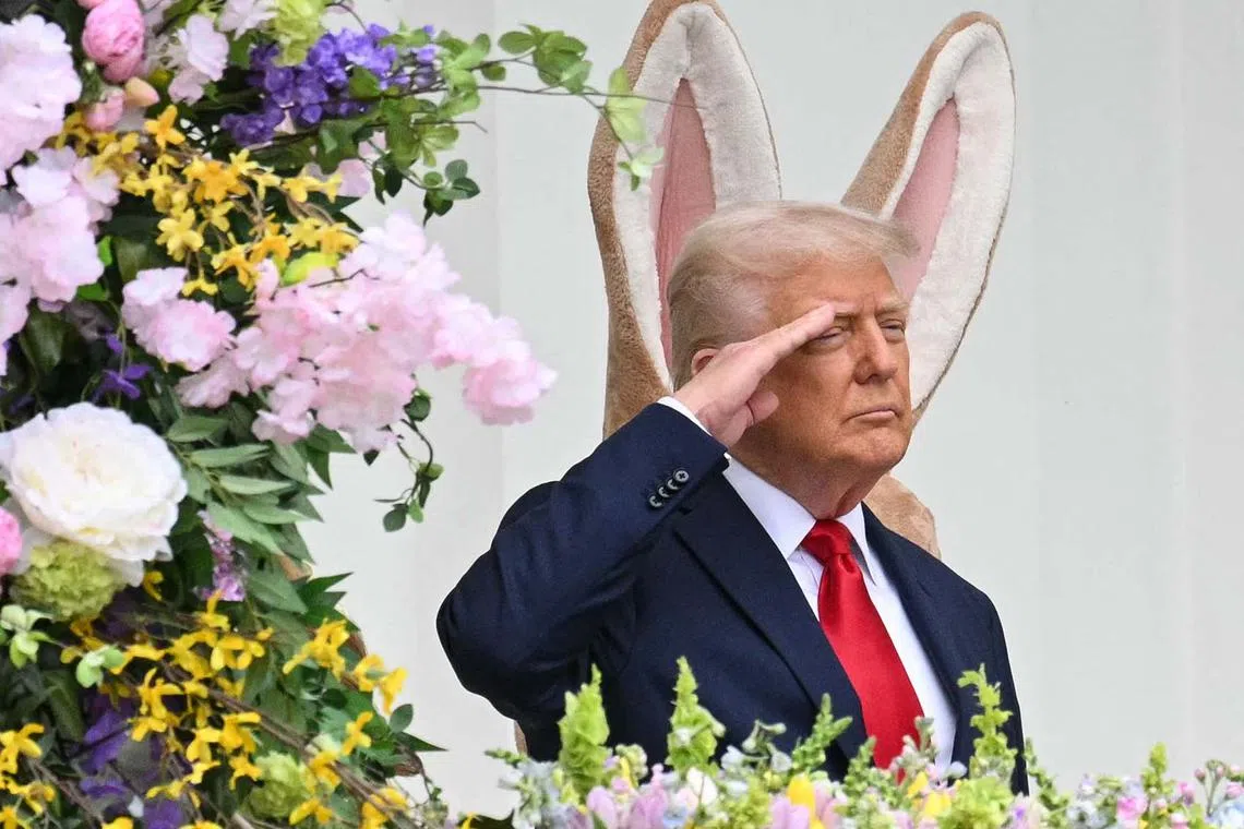 TOPSHOT - An Easter bunny stands behind US President Donald Trump as Trump salutes on the Blue Room Balcony during the annual Easter Egg Roll on the South Lawn of the White House on April 21, 2025, in Washington, DC. According to the US National Park Service, the egg roll tradition dates back to 1878 when President Rutherford B. Hayes invited children to roll Easter eggs on the White House grounds. Children previously rolled eggs down a hill at the US Capitol in the early 1870s, but a law was passed in 1876 forbidding the Capitol property from being used due to the toll on the lawn. (Photo by Mandel NGAN / AFP)