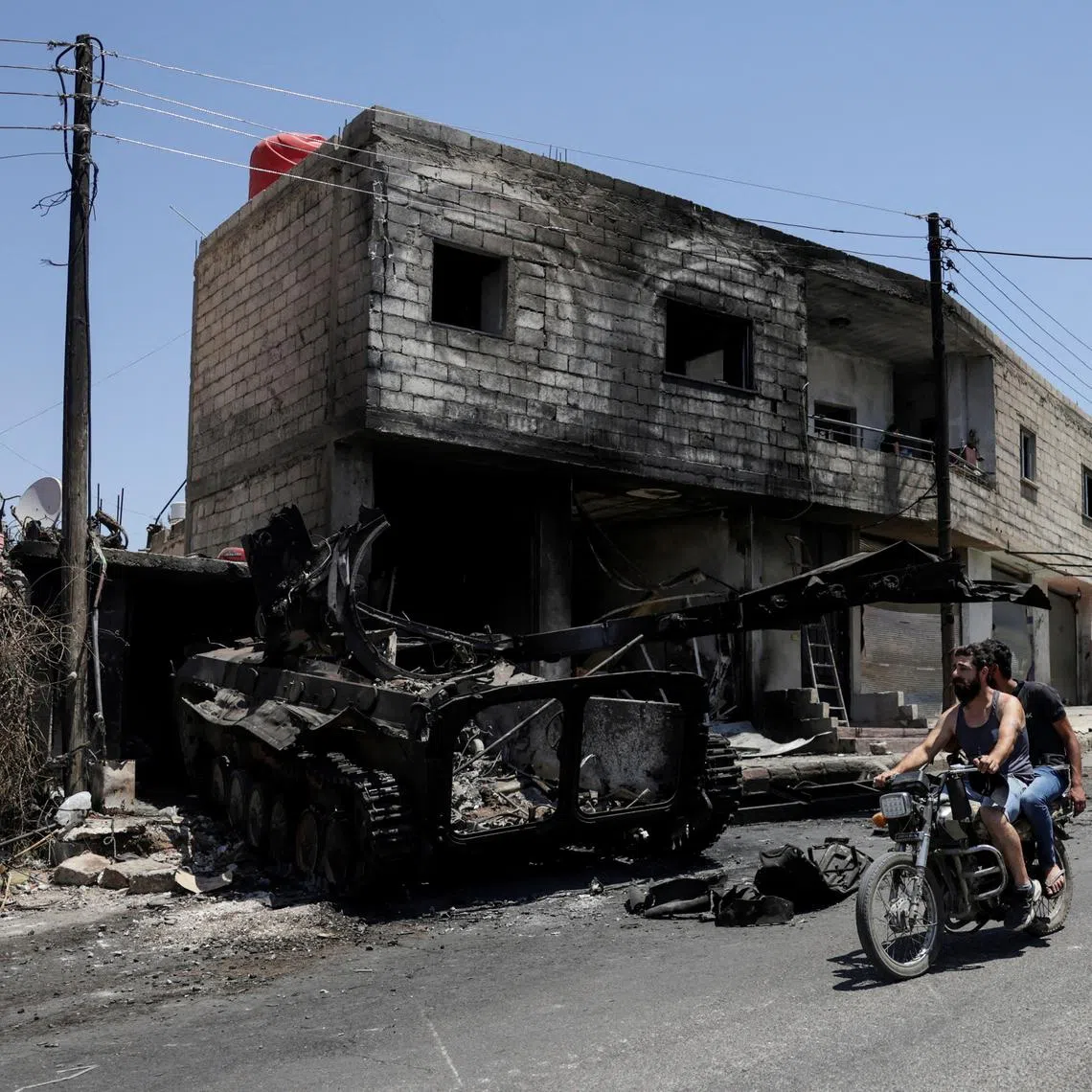 FILE PHOTO: People ride a motorcycle past a burned-out military vehicle, following deadly clashes between Druze fighters, Sunni Bedouin tribes and government forces, in Syria's predominantly Druze city of Sweida, Syria July 25, 2025. REUTERS/Khalil Ashawi/File Photo