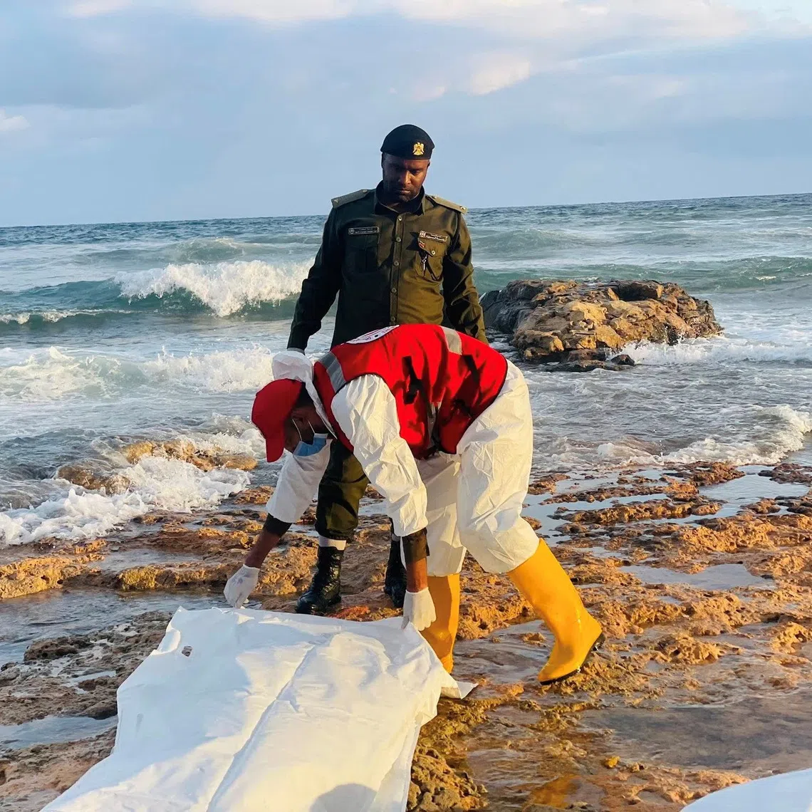 A member of the Red Crescent holds a body bag next to a member of the military in a location given as near Surman, Libya, after a migrant boat capsized west of Libya's capital Tripoli, in this handout image released on October 28, 2025. Libyan Red Crescent Society in Sabratha/Handout via REUTERS