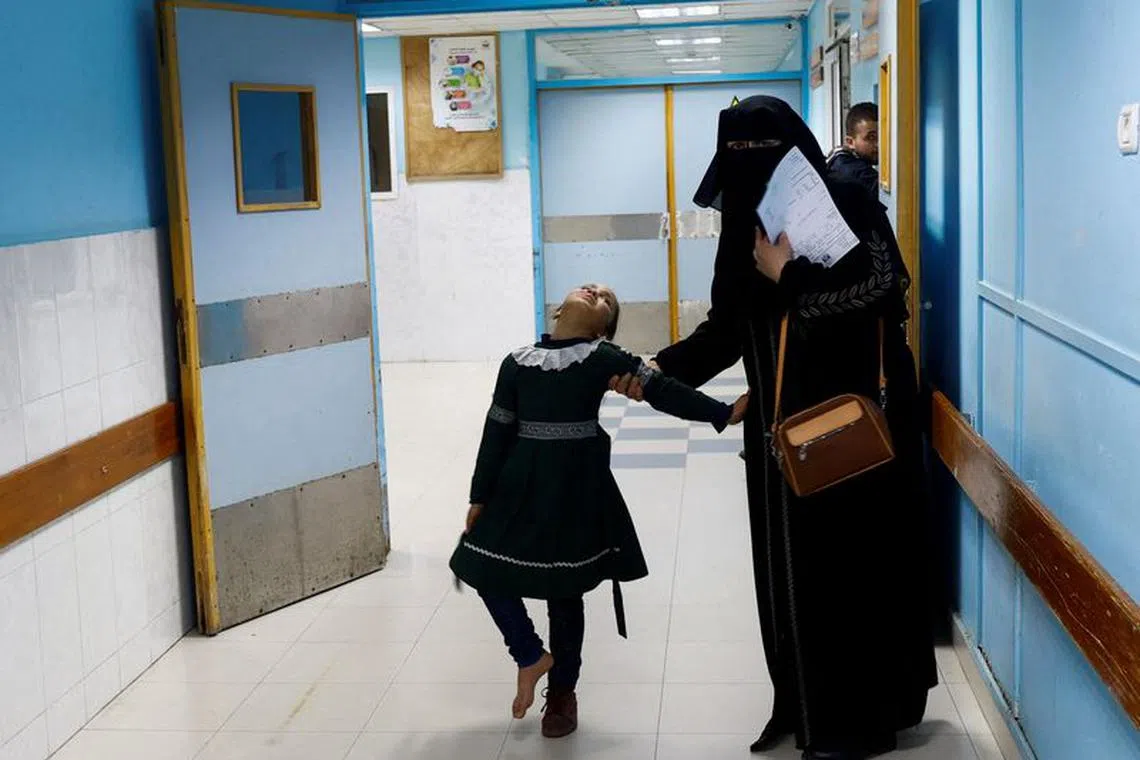 A Palestinian woman helps a school girl walk at the X-ray unit in Shifa hospital in Gaza City, January 5, 2023. REUTERS/Ibraheem Abu Mustafa