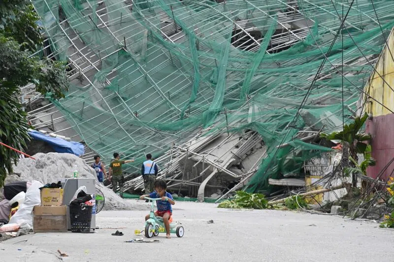 A child riding a tricycle next to a collapsed building in Angeles City, north of Manila, where at least 12 people were believed to be buried.