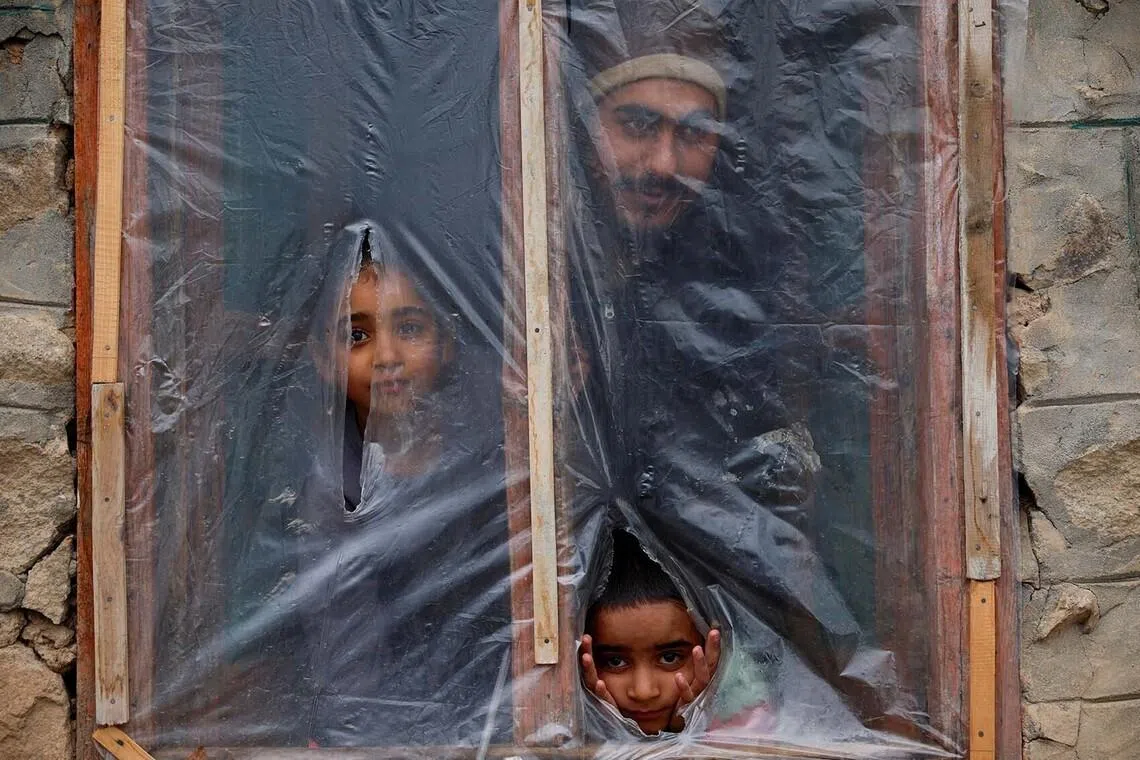 A Kashmiri family looking out from a window covered with a plastic sheet used to protect them from the cold in the hamlet of Faqir Gujri on the outskirts of Srinagar, Indian Kashmir, Febr 2, 2026. 