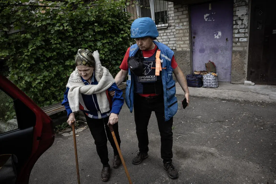 FILE — Yevhen Tkachov, a volunteer with the Ukrainian aid group Proliska helping Tetiana Chubina, 74, to a car as she evacuated from Kostiantynivka, Ukraine, June 20, 2025. Moscow wants Ukraine to unilaterally withdraw from the entire eastern region known as the Donbas. For a variety of military, humanitarian and political reasons, Ukrainians find it difficult to imagine. (David Guttenfelder/The New York Times)