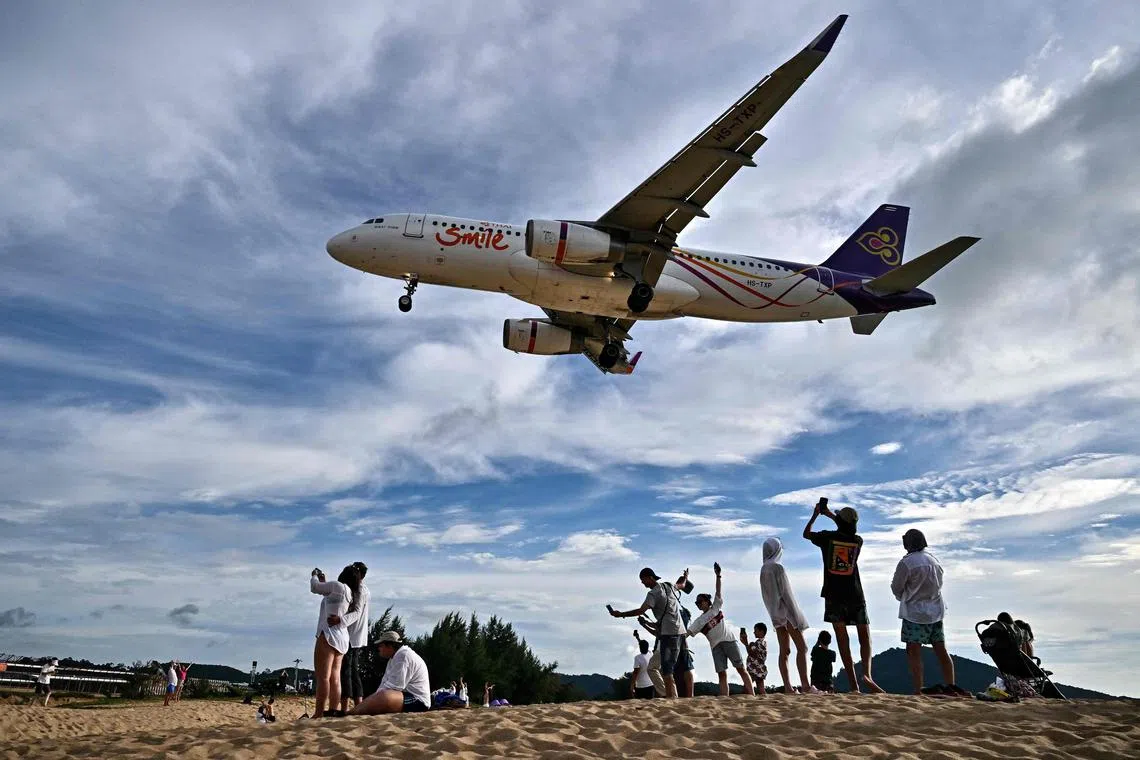 Tourists posing for pictures on Thailand's Mai Khao Beach as an airplane lands at the Phuket International Airport.