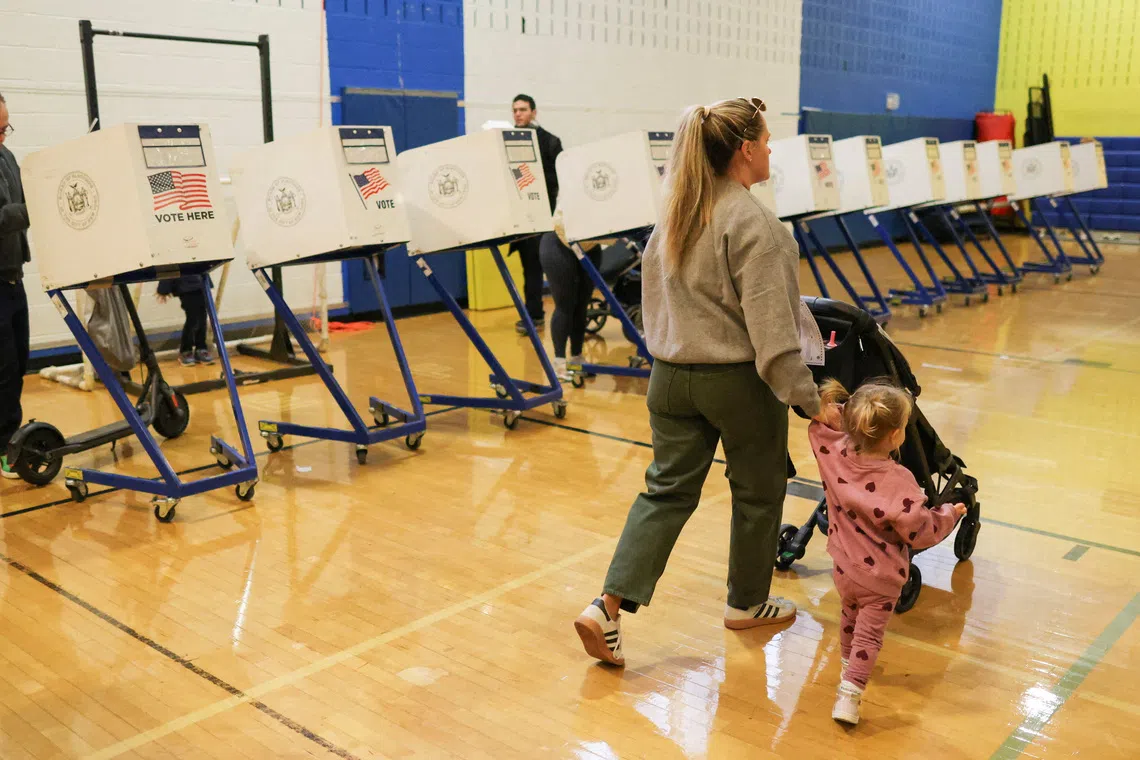 FILE PHOTO: A woman a her child walk past voting booths during the New York City mayoral election, at a polling site at the High School of Art and Design in the Manhattan borough of New York City, U.S., November 4, 2025. REUTERS/Brendan McDermid/File Photo