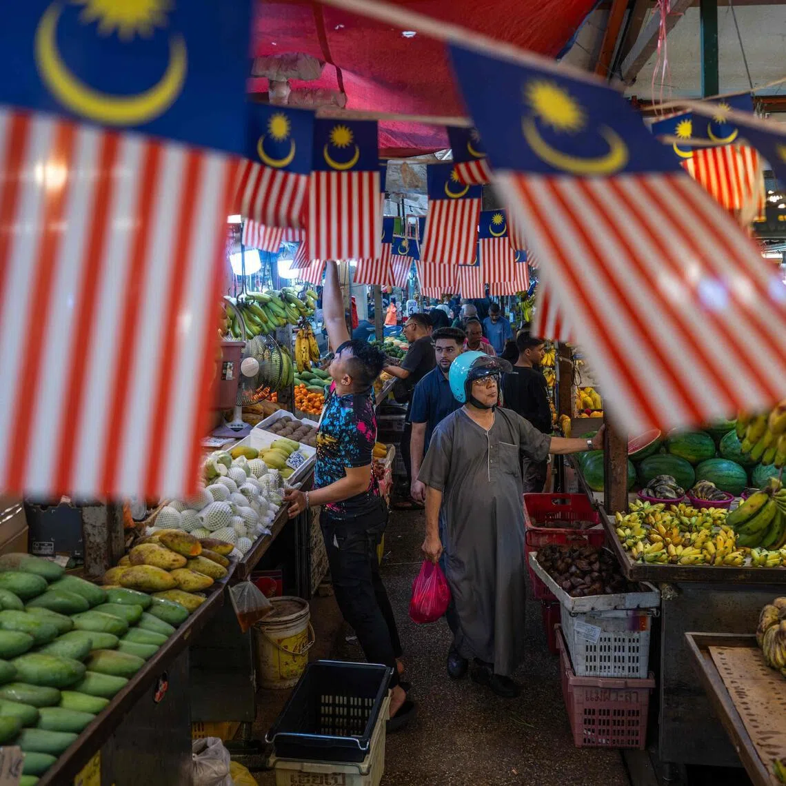 People browse for produce under Malaysian national flags at a fruit market in Kuala Lumpur on April 28.