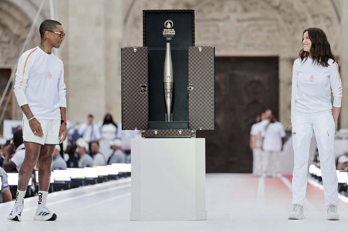 TOPSHOT - US rapper, artist and designer Pharell Williams (L) and French actress Laetitia Casta (R) stand next to a trunk containing the Olympic torch as part of the 2024 Paris Olympic Games Torch Relay, on the day of the opening ceremony, in Saint-Denis, outside Paris, on July 26, 2024. (Photo by STEPHANE DE SAKUTIN / POOL / AFP)