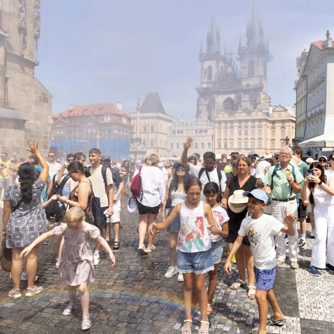 People are sprayed with water to cool down during a hot, sunny day at Old Town Square in Prague, Czech Republic.