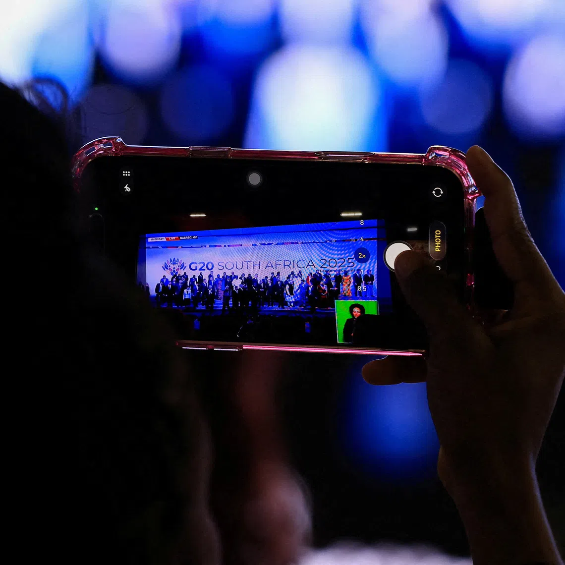 A person uses their phone to capture the leaders family photo on a big screen, on the opening day of the G20 leaders' Summit at the Nasrec Expo Centre in Johannesburg, South Africa, November 22, 2025. REUTERS/Esa Alexander/File Photo