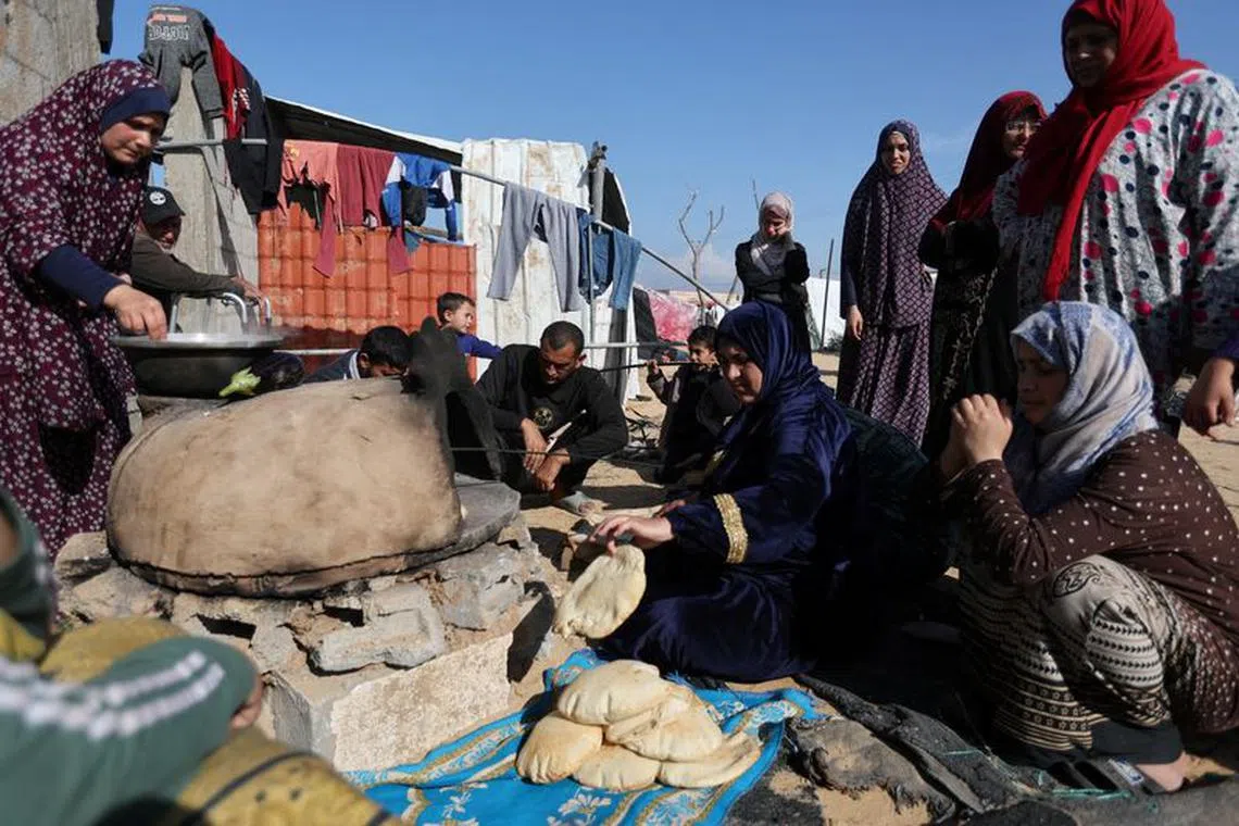 People wait while a woman prepares food, as displaced Palestinians, who fled their houses due to Israeli strike, shelter in a camp in Rafah, amid the ongoing conflict between Israel and Palestinian Islamist group Hamas, in the southern Gaza Strip, December 6, 2023. REUTERS/Ibraheem Abu Mustafa