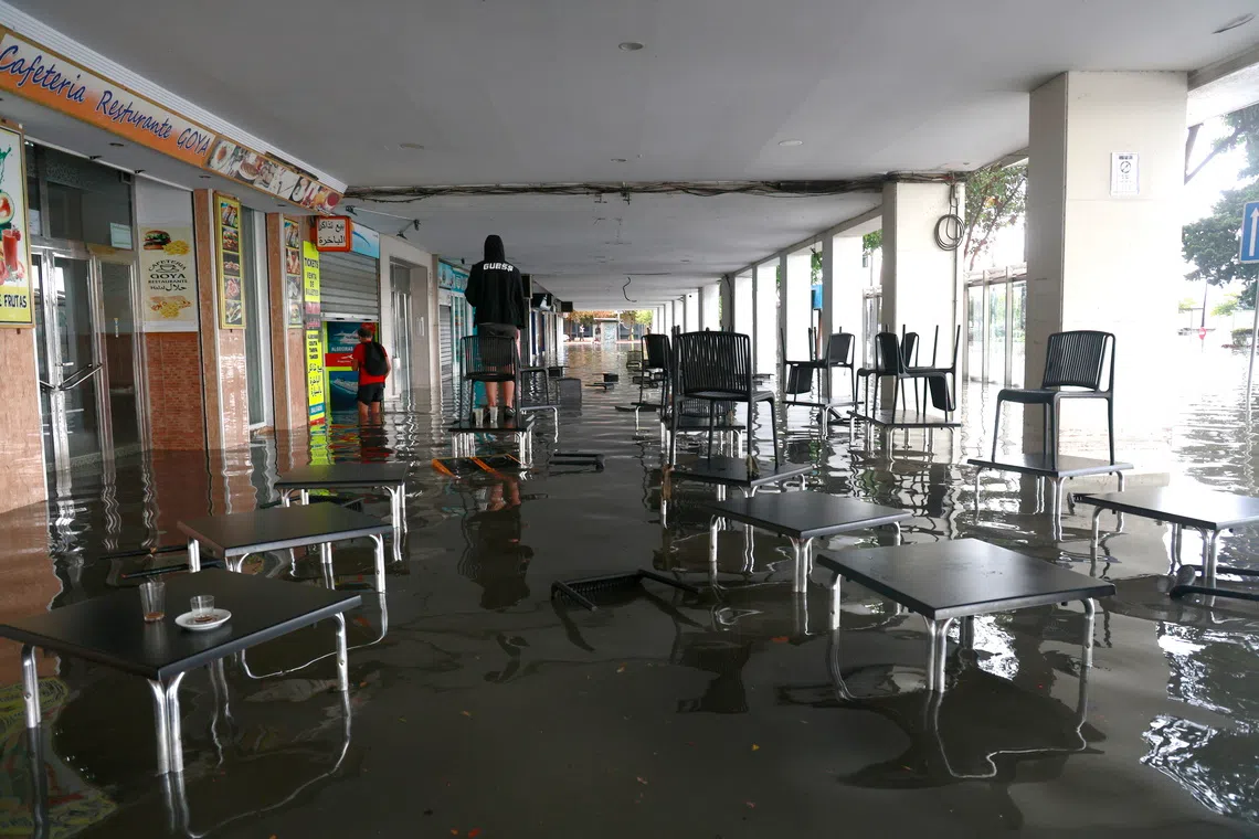 A resident stands on a bar table at a flooded street after heavy rainfall that hit the area early in the morning, in the town of Algeciras, southern Spain, on Oct 18.