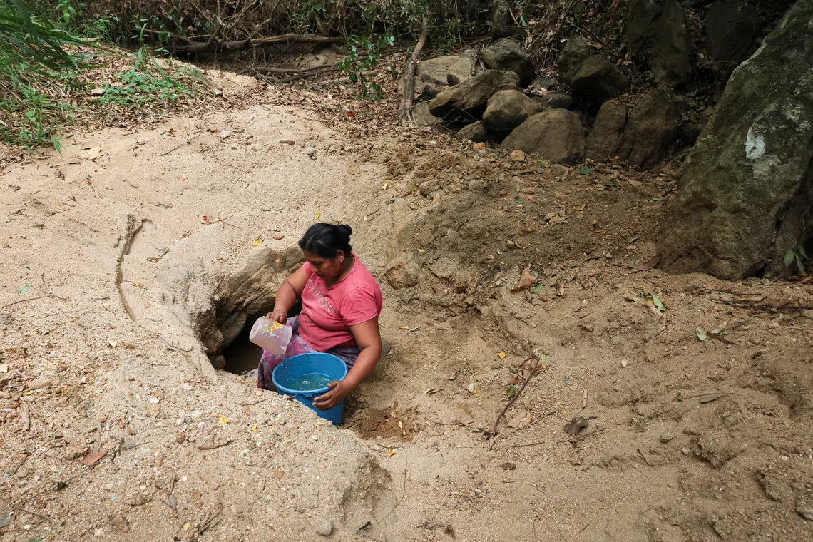 A woman draws water from a hole dug in a dry riverbed using a mug in Monaragala district, Sri Lanka, August 24, 2026. REUTERS/Priyanshu Singh
