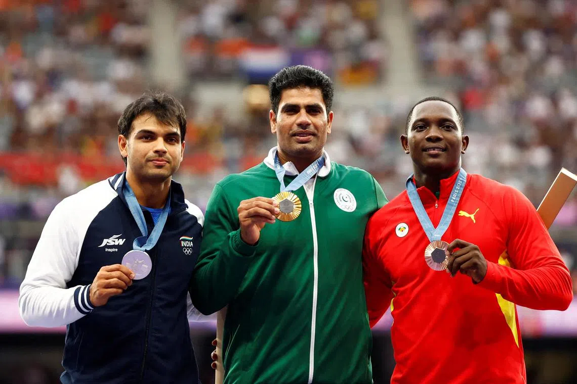 Gold medallist Arshad Nadeem of Pakistan celebrates with his medal on the podium with silver medallist Neeraj Chopra of India and bronze medallist Anderson Peters of Grenada.