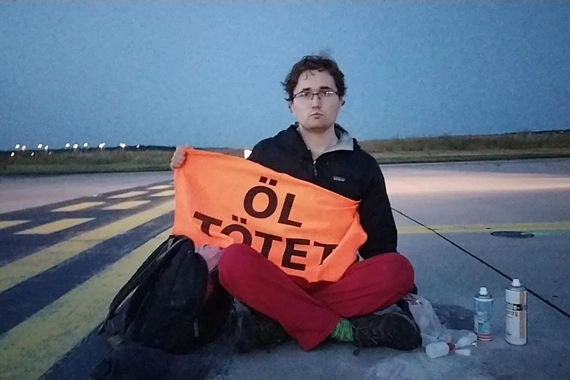 A Last Generation activist with a banner reading 'Oil kills' and his hand glued to the ground of a runway at the airport in Frankfurt.