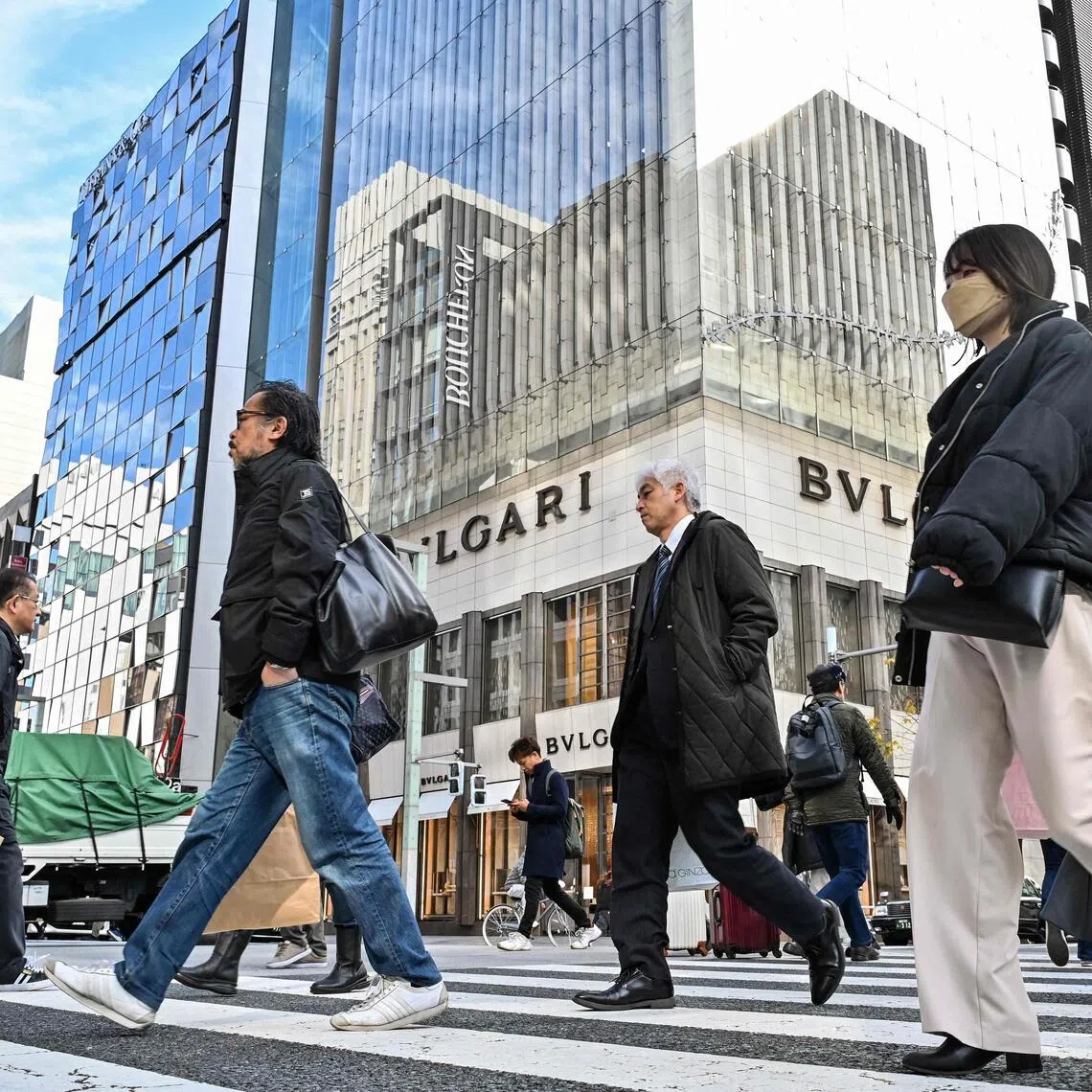 Pedestrians cross the street in front of luxury shops at the Ginza shopping district in Tokyo on January 19, 2024. Japanese consumer inflation slowed again in December due to lower electricity and gas bills, government data showed on January 19, ahead of a Bank of Japan policy decision next week. (Photo by Richard A. Brooks / AFP)