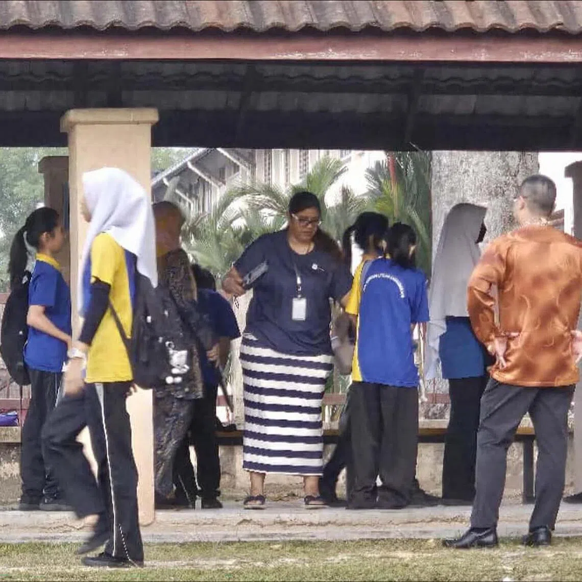 A teacher from SMK Bandar Utama Damansara 4 uses a metal detector to screen students before they enter the school compound