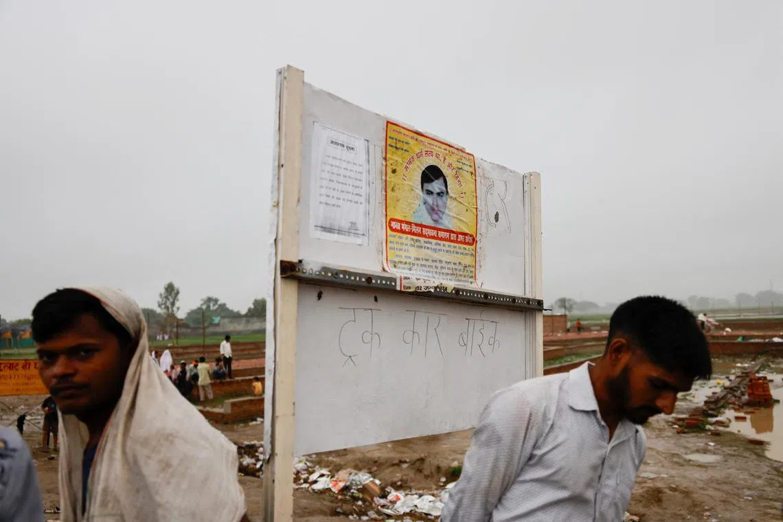 People stand near a poster of preacher Surajpal, also known as 'Bhole Baba stuck on a board, at the site where believers had gathered for a Hindu religious congregation following which a stampede occurred, in Hathras district of the northern state of Uttar Pradesh, India, July 3, 2024. REUTERS/Anushree Fadnavis