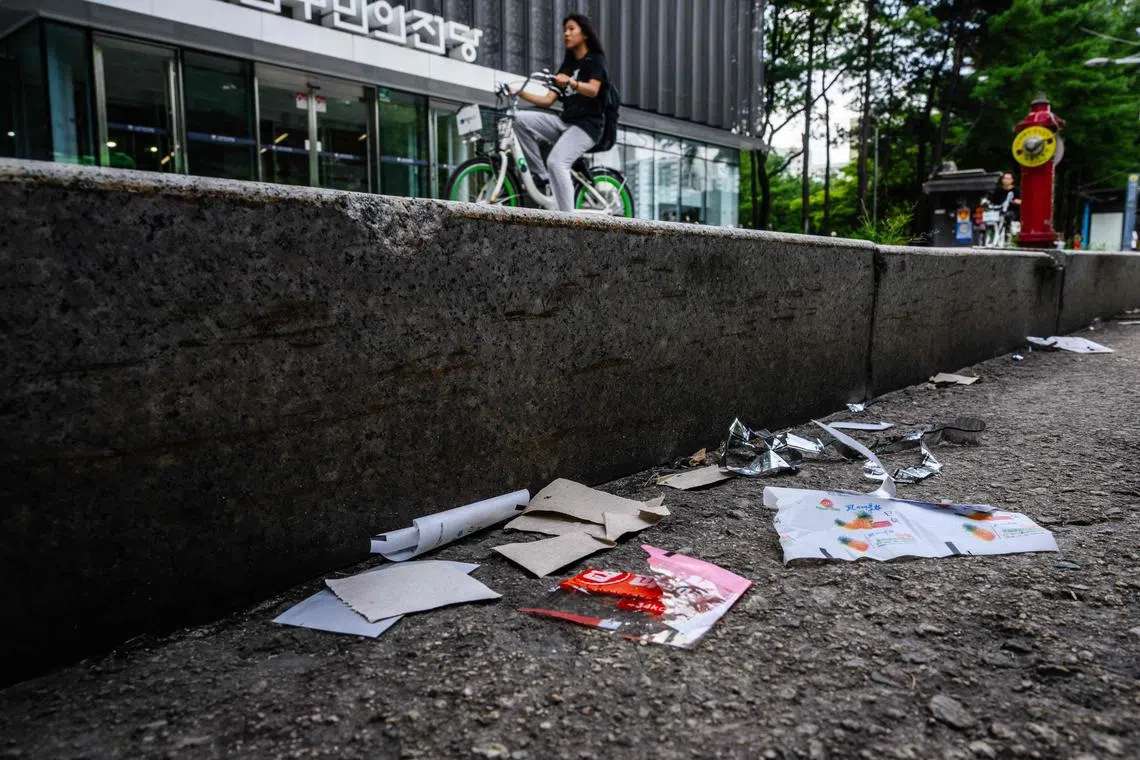 A woman cycles along a pavement past pieces of North Korean food packaging, sweet wrappers and paper suspected to be from trash balloons sent from North Korea, in Seoul on July 24, 2024. North Korean sweet wrappers and packets of crackers and other snacks made at a factory once visited by leader Kim Jong Un were found by AFP reporters on Seoul streets on July 24. (Photo by Anthony WALLACE / AFP)