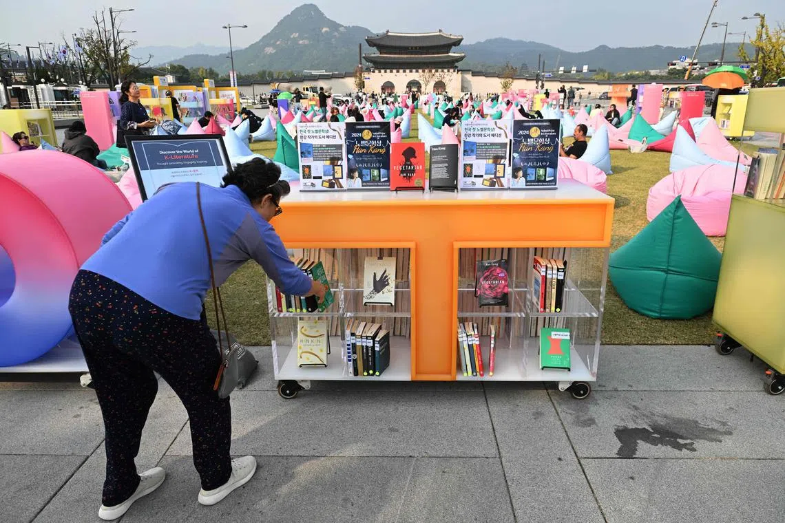 A woman picks up a book by South Korean author Han Kang, who won the 2024 Nobel Prize in Literature, displayed during an outdoor library event at Gwanghwamun square in central Seoul on October 11, 2024. From the president to K-pop megastars BTS, South Korea erupted into celebration on October 10, after "The Vegetarian" author Han Kang won the country's first Nobel Prize for literature. (Photo by Jung Yeon-je / AFP)