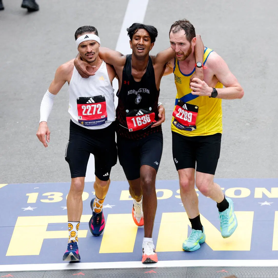 Mr Ajay Haridasse (centre) is helped by fellow runners Robson Oliveira (left) and Aaron Beggs across the finish line at the 2026 Boston Marathon on April 20. 