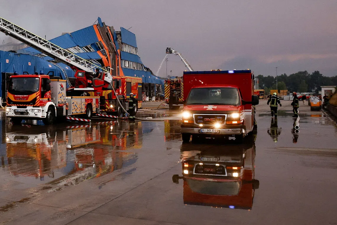 Emergency vehicles parked in front of a large blue industrial building on a wet street.
