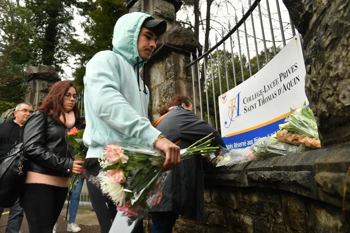 People place flowers at the entrance to Saint-Thomas d’Aquin middle school in France, where a teacher died after being stabbed by a student, on Feb 23, 2023.