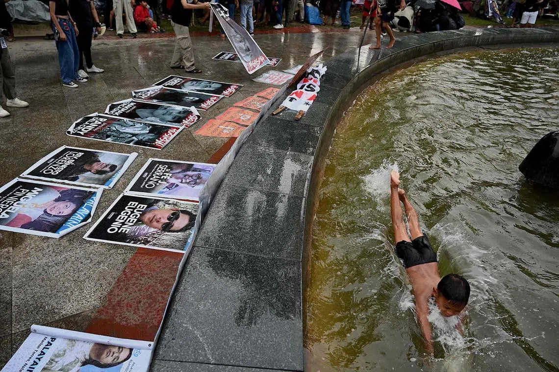 A child swims in a fountain as protesters display photos of Martial Law victims during a protest commemorating the 51st anniversary of the imposition of Martial Law, at Liwasang Bonifacio in Manila on September 21, 2023. (Photo by JAM STA ROSA / AFP)