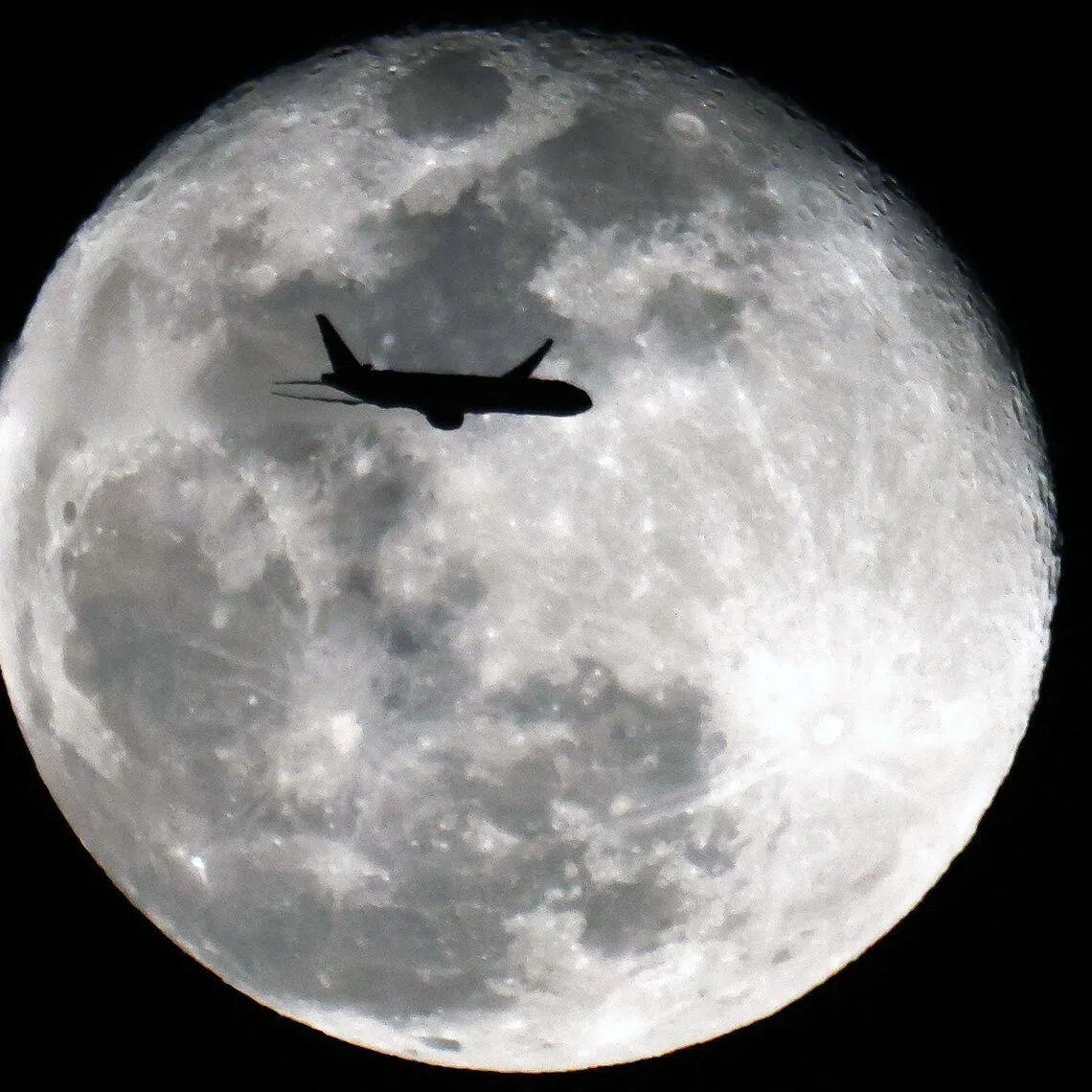 TOPSHOT - An Boeing 777-369 (ER) Kuwait Airways aircraft headed to Mumbay, India, is silhouetted against the Waning Gibbous moon above Kuwait City on January 4, 2026. (Photo by YASSER AL-ZAYYAT / AFP)