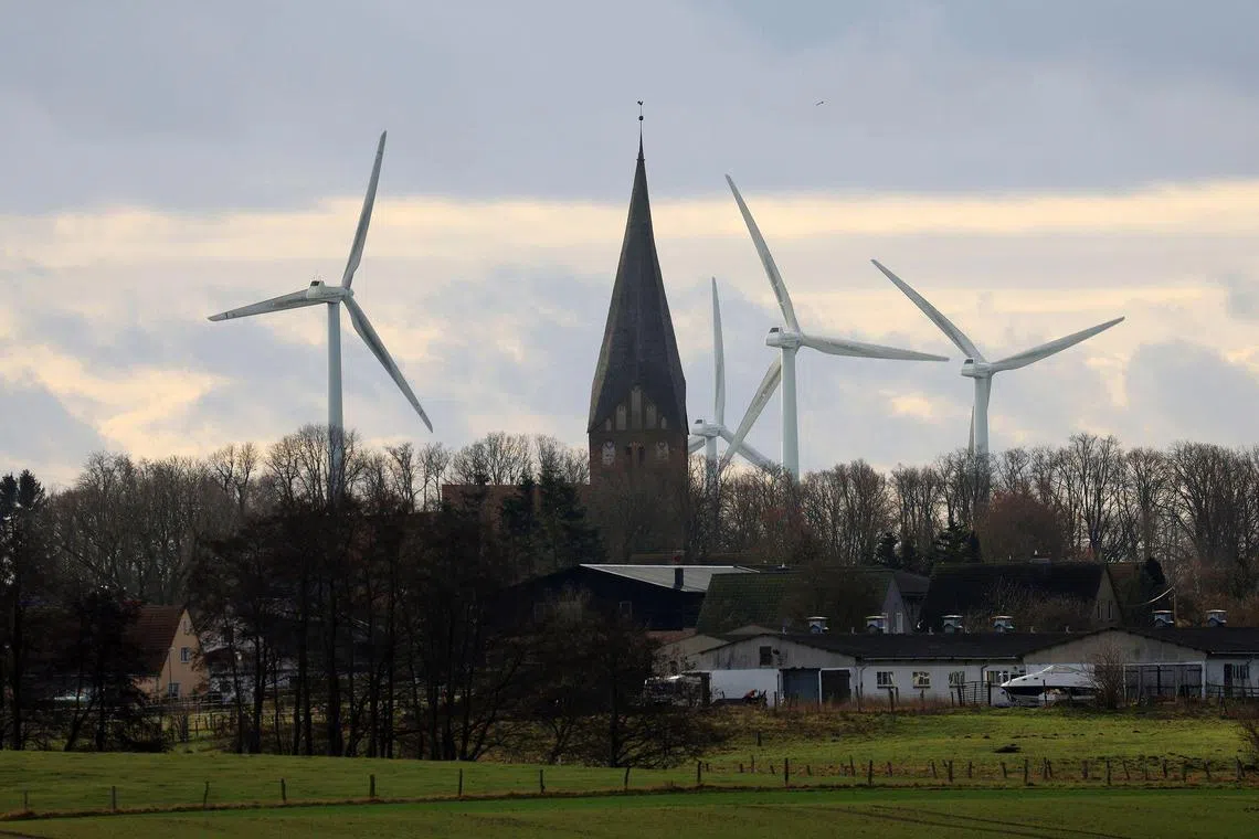 Wind turbines beyond housing and a church near Wusterhusen, Germany, on Saturday Jan. 14, 2023. Chancellor Olaf Scholz said Germany needs to increase its pace of expanding renewable power to reach its goal of becoming climate-neutral by 2045, even as Europe's largest economy withstands the initial impact of Russia's energy squeeze. Photographer: Krisztian Bocsi/Bloomberg