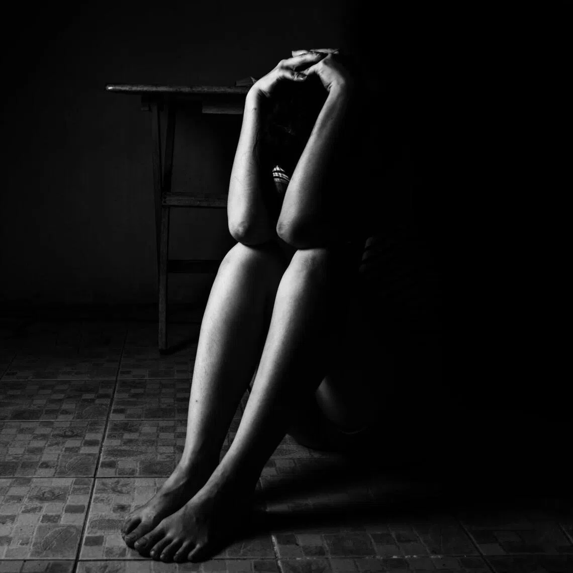 a woman sitting on ground with arm around lower head, sexual violence , sexual abuse, human trafficking concept with shadow edge in white tone..