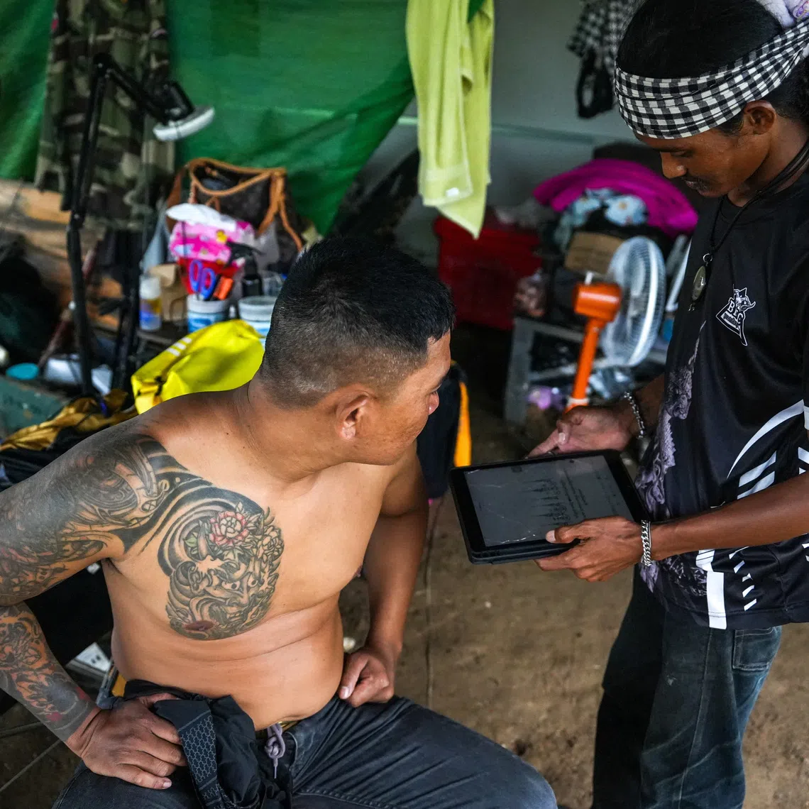 Tattoo artist Cheng Bora speaks with a customer at his house in Rong Cham, a resettlement site villagers have nicknamed \"the waiting village\", home to families who fled fighting along the Cambodia-Thailand border and are waiting for a chance to return, in Banteay Meanchey province, Cambodia, September 15, 2026. REUTERS/Soveit Yarn