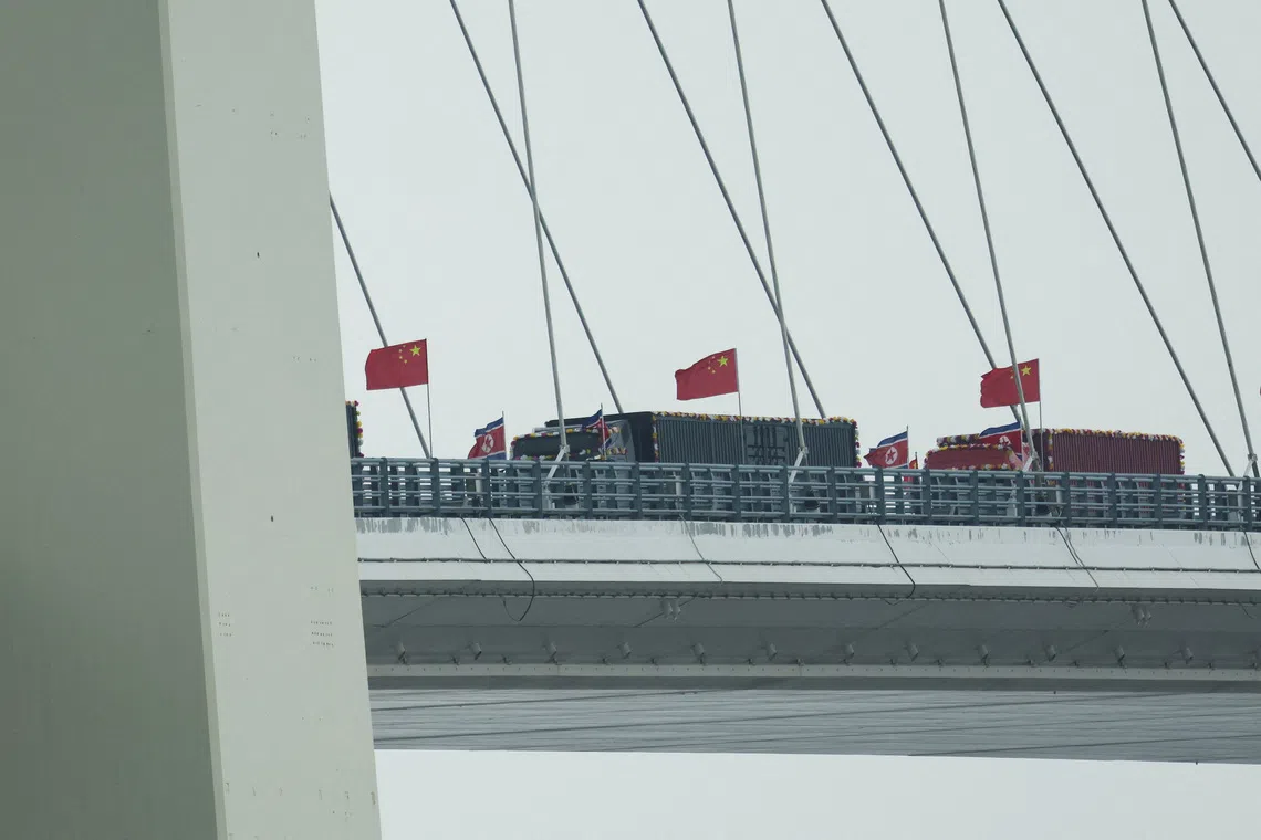 Trucks adorned with North Korean flags enter the Chinese side of the newly opened New Yalu River Bridge on Oct 15.