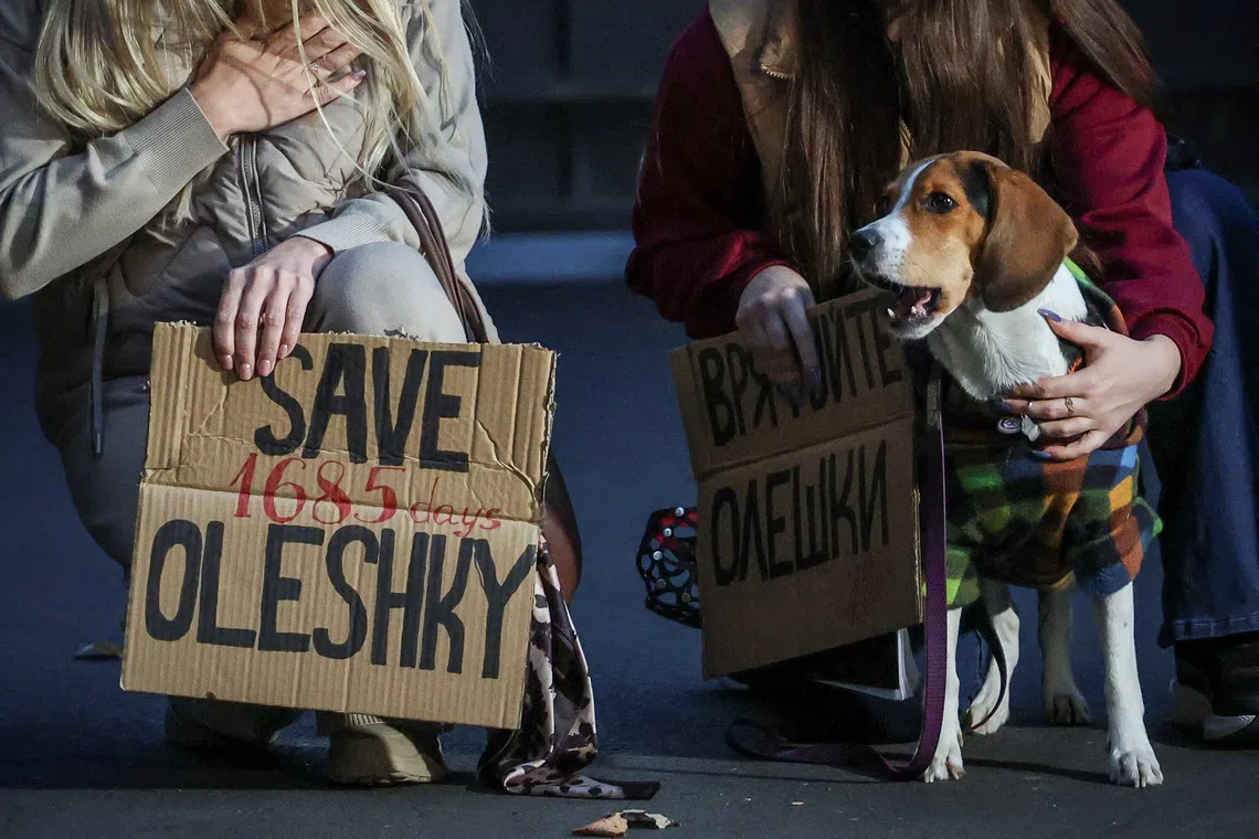 A dog looks on while women hold posters in Kyiv as they participate in a rally demanding the establishment of a humanitarian corridor to evacuate Ukrainian civilians from the town of Oleshky in Kherson region, Ukraine, on Oct 6.