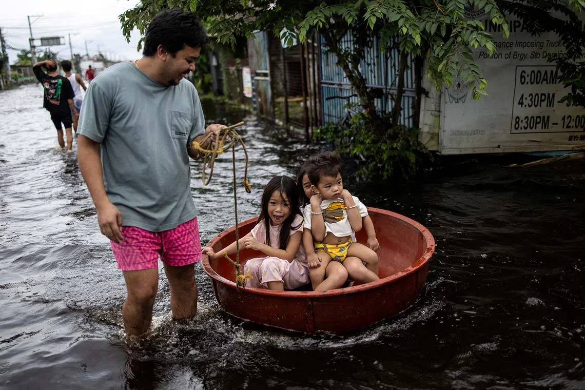 Children sitting in a basin reacting as they are pulled through a flooded area on Manila North Road following heavy rains brought by Typhoon Co-may in Minalin, Pampanga, Philippines, July 25, 2025. 