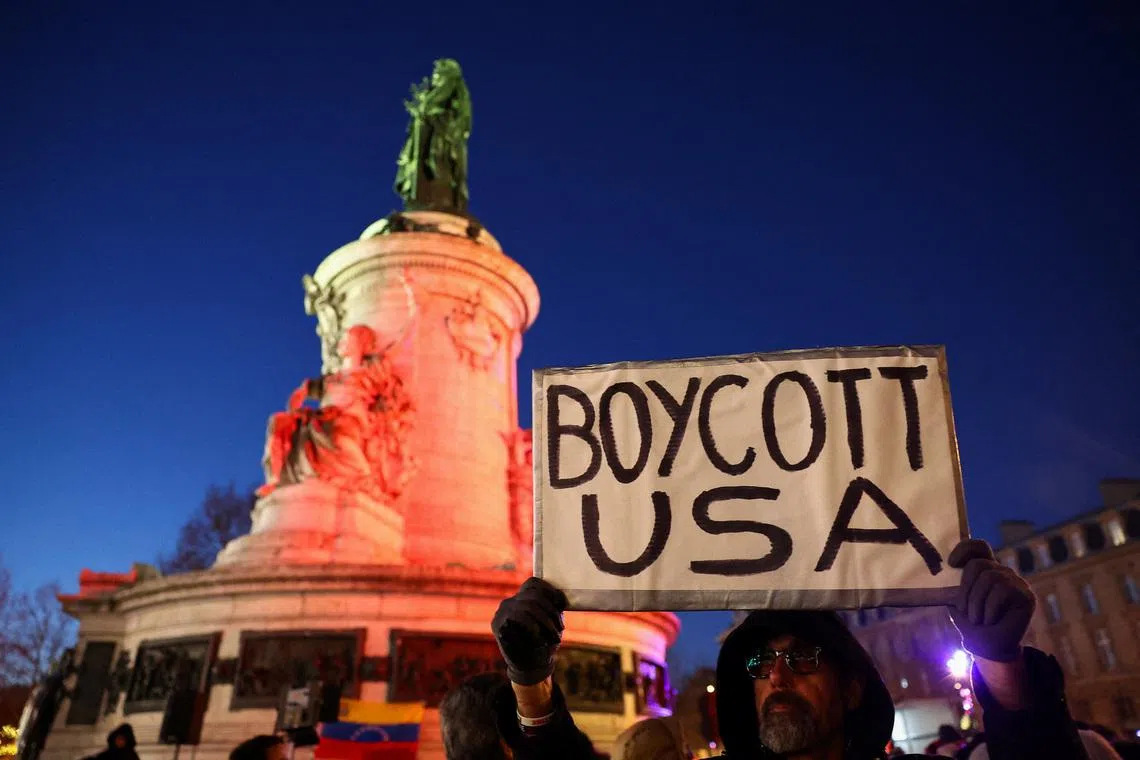 A man holds up 'Boycott USA' sign, as people demonstrate to oppose U.S. actions in Venezuela at a protest, after U.S. President Donald Trump said the U.S. has struck Venezuela and captured its President Nicolas Maduro, in Paris, France, January 3, 2026. REUTERS/Abdul Saboor