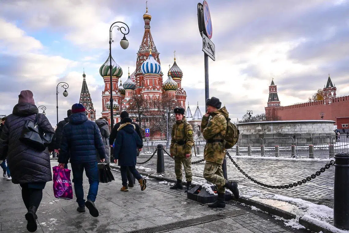 Pedestrians walk past two soldiers as they stand at the Red Square near the Saint Basil's Cathedral in Moscow, on Nov 18, 2022. 
