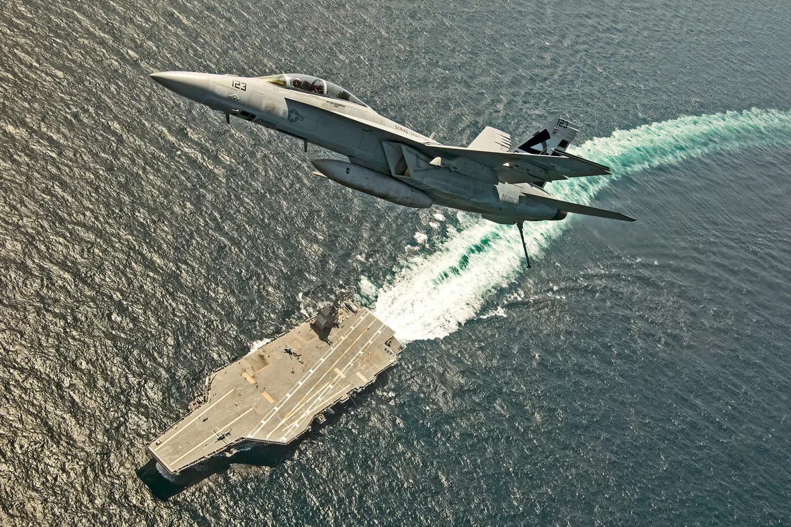 FILE PHOTO: An F/A-18F Super Hornet jet flies over the USS Gerald R. Ford as the U.S. Navy aircraft carrier tests its EMALS magnetic launching system, which replaces the steam catapult, and new AAG arrested landing system in the Atlantic Ocean July 28, 2017. U.S. Navy/Erik Hildebrandt/Handout via REUTERS/File Photo