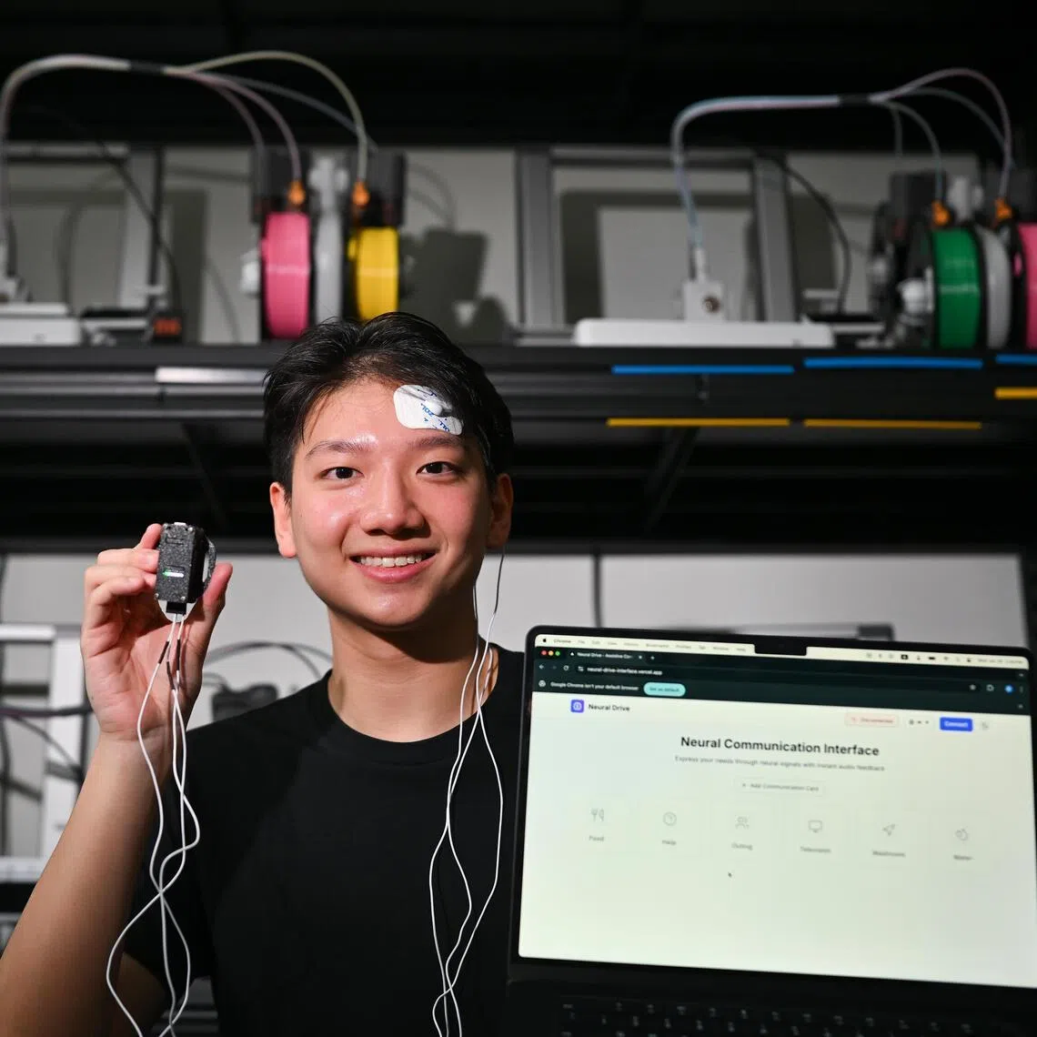 Mr Raymond Ng, 21, Chief AI Officer of Neural Drive, wearing the electrodes and holding the headset with the laptop showing the interface of Neural Drive.