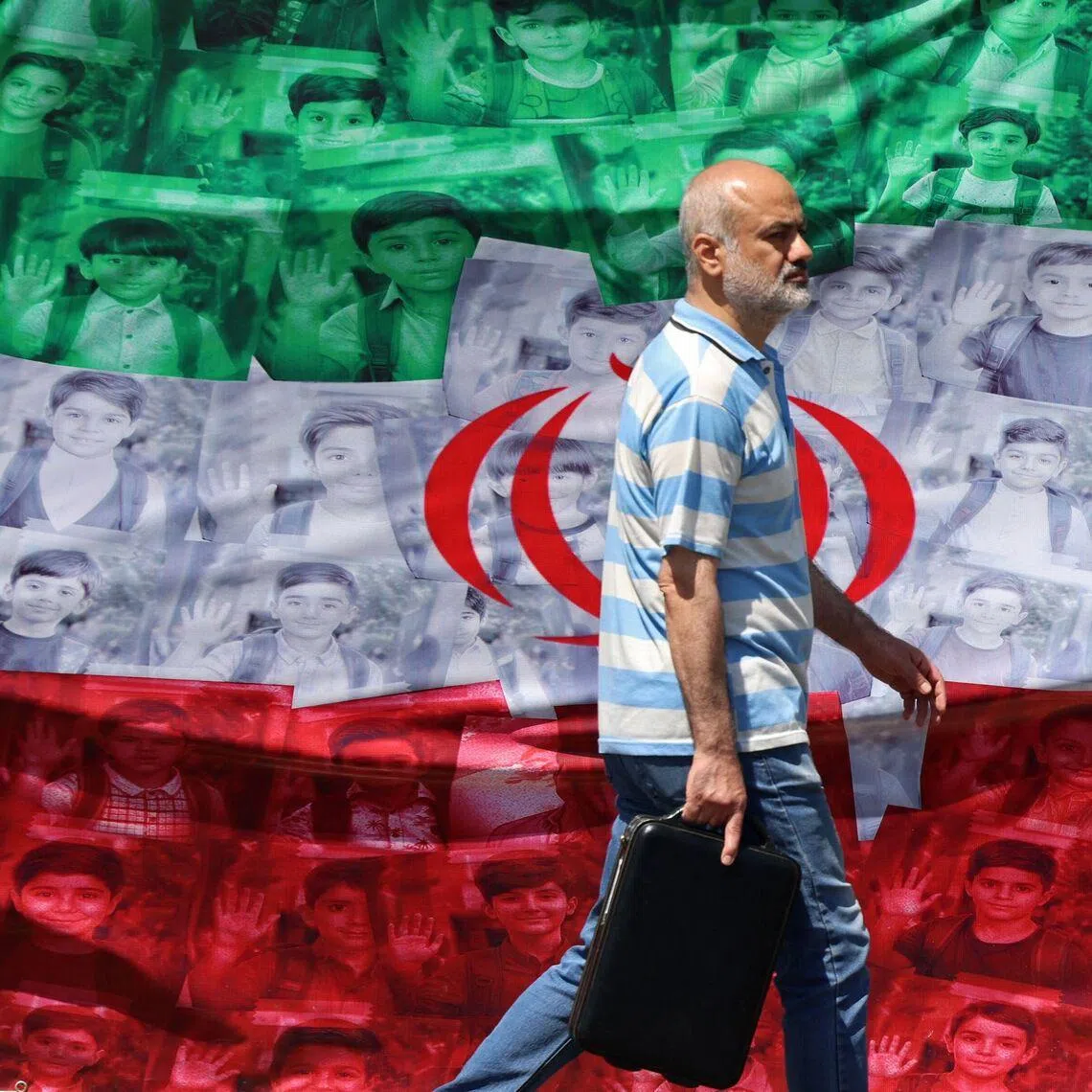 A man walks past an Iranian flag depicting images of children killed on the first day of the war.