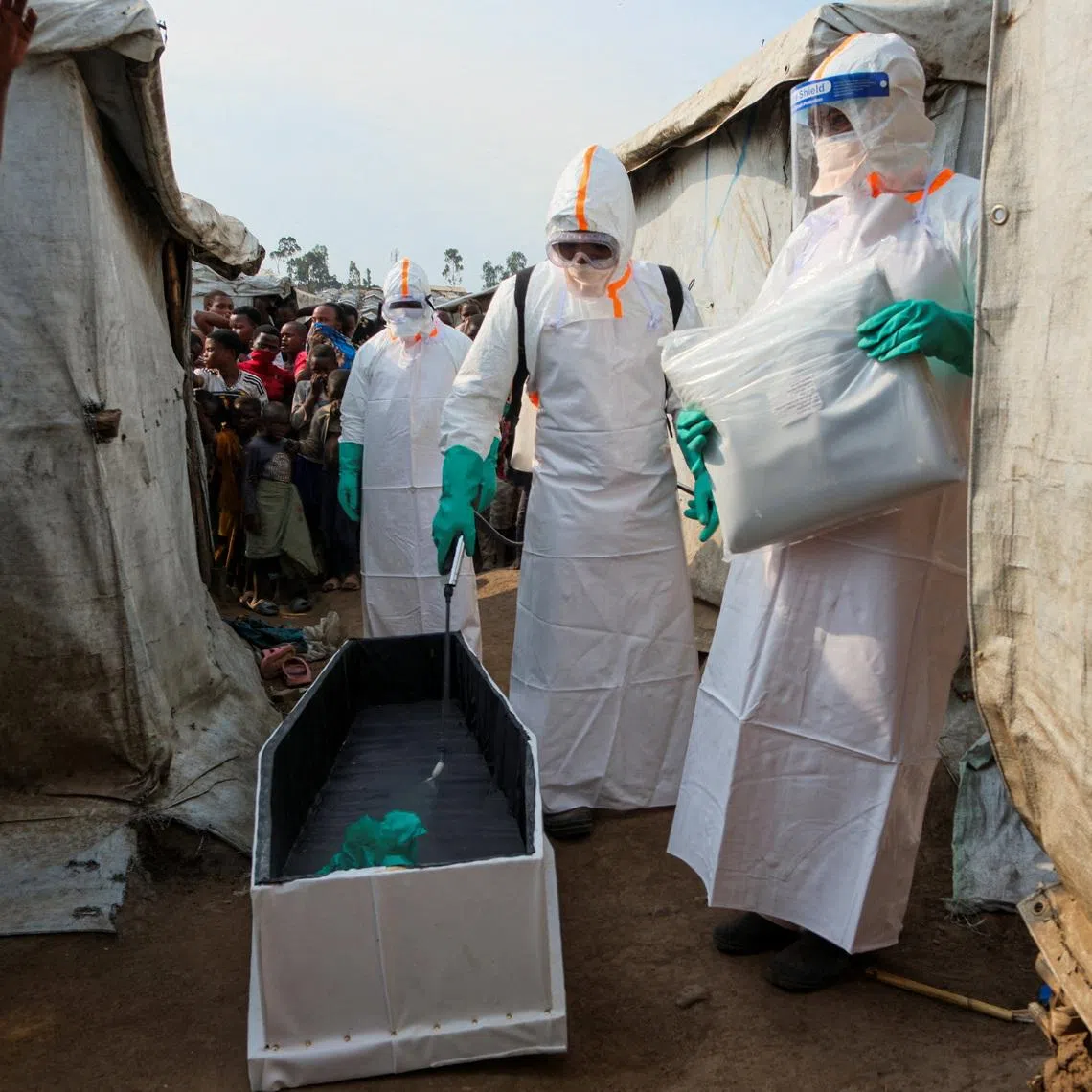 Health workers in full personal protective equipment disinfect a coffin while preparing for the burial of suspected Ebola victims.