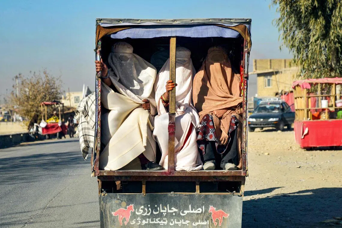 TOPSHOT - Afghan burqa-clad women ride on the back of a vehicle, in Kandahar on December 29, 2024. (Photo by Sanaullah SEIAM / AFP)