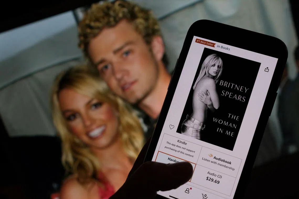 This illustration image taken on October 21, 2023 shows the cover of Britney Spears' book The Woman In Me from an online retailer in front of a picture of Britney Spears and Justin Timberlake at the American Music Awards from Jan 9, 2002. 