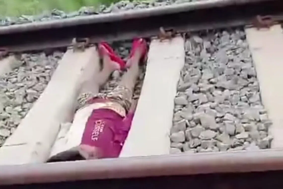In the video, the boy is seen lying between rails as a train speeds by.
