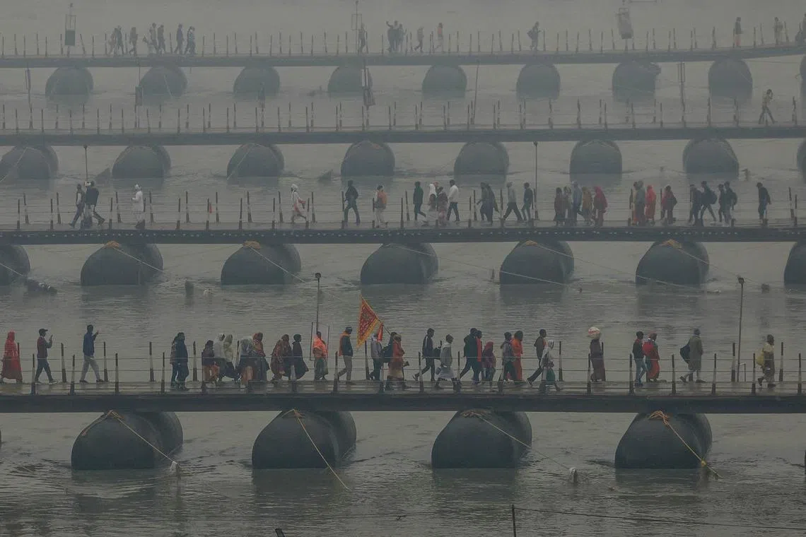 TOPSHOT - Hindu pilgrims carrying their belongings walk over floating pontoon bridges to go to Sangam, the confluence of the Ganges, Yamuna and mythical Saraswati rivers, on a foggy winter evening to take part in the Maha Kumbh Mela festival in Prayagraj on January 12, 2025. The millennia-old Kumbh Mela, a sacred show of religious piety and ritual bathing that opens January 13, is held at the site where the holy Ganges, Yamuna and the mythical Saraswati rivers meet. (Photo by Niharika KULKARNI / AFP)