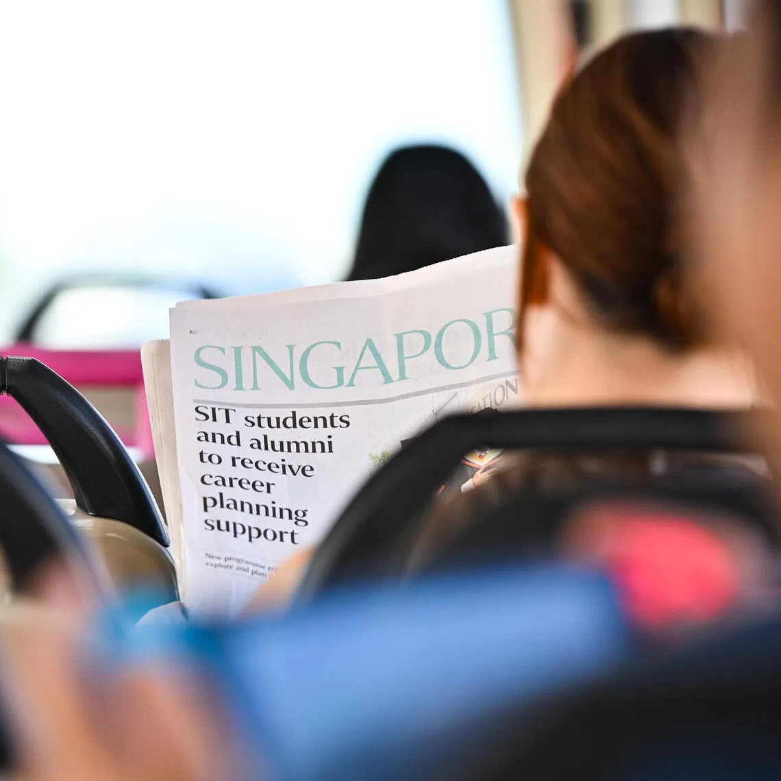 A passenger reading a copy of The Straits Times newspaper on the bus.